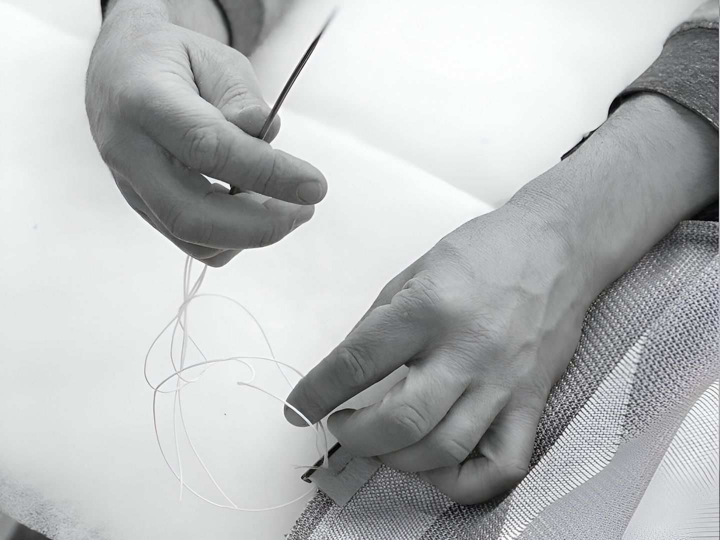 Schwarz-weiß-Foto einer Person, die eine Nadel in der Hand hält, symbolisiert Präzision und Handwerkskunst.