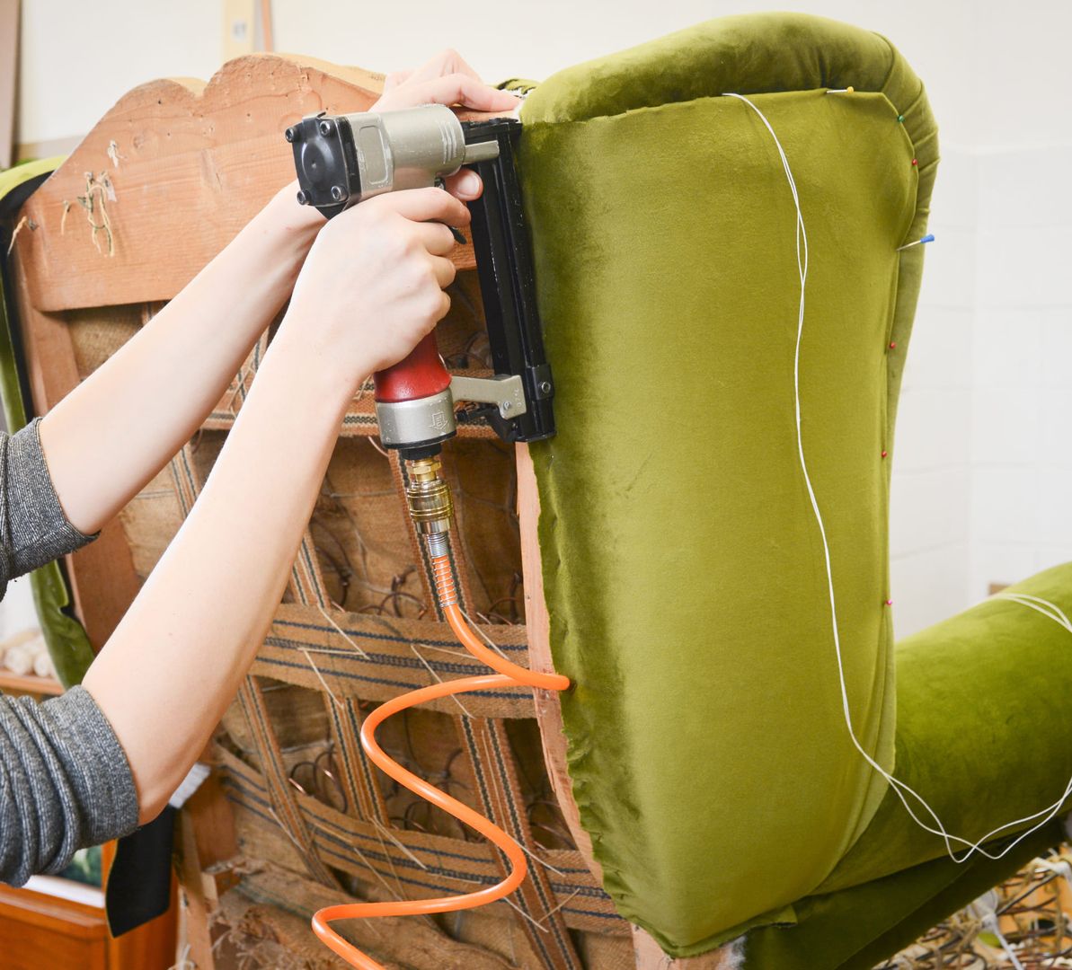 Eine Frau verwendet eine Nagelpistole, um einen Stuhl zu reparieren, während sie konzentriert arbeitet.